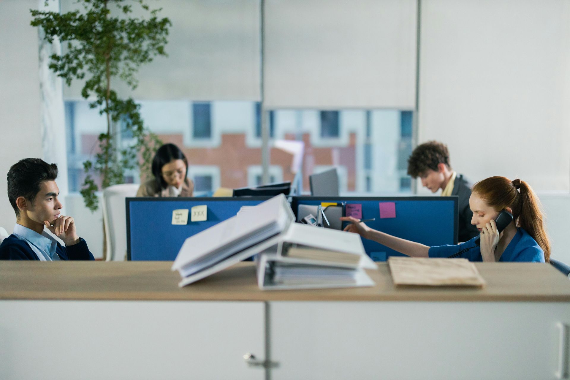 Office workers seated at desks in a bright open-plan workspace, with laptops and papers in the foreground