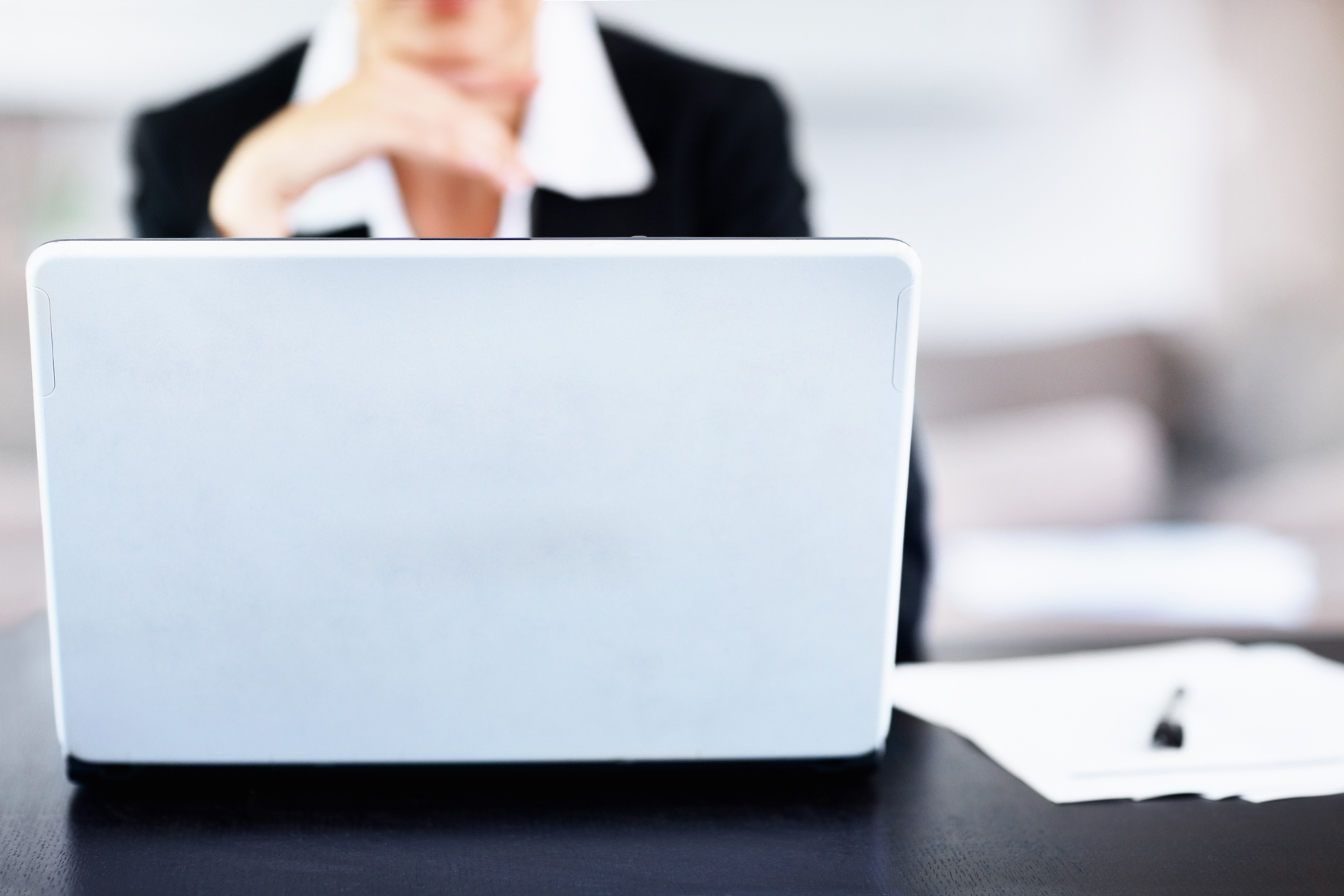 Person behind open laptop at desk with a pen and paper nearby