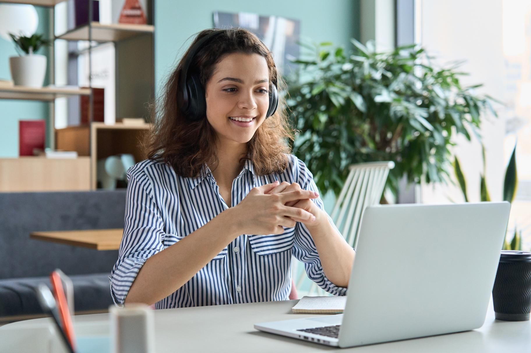 A woman wearing headphones is sitting at a table using a laptop computer.