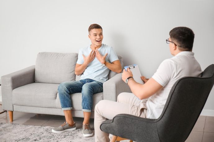 A young man is sitting on a couch talking to a psychologist.