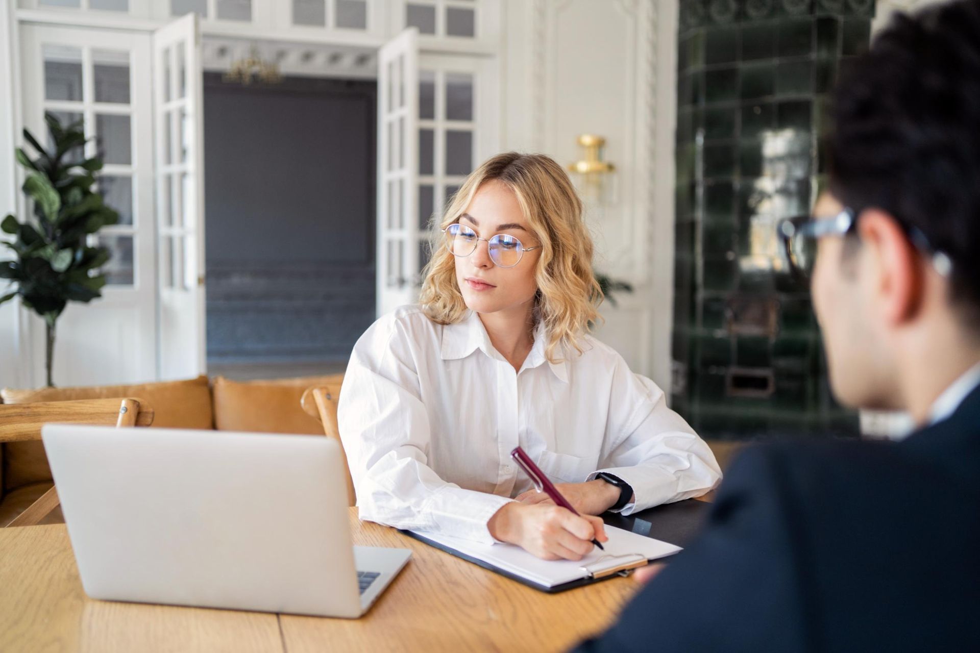 A woman is sitting at a table talking to a man with a laptop.