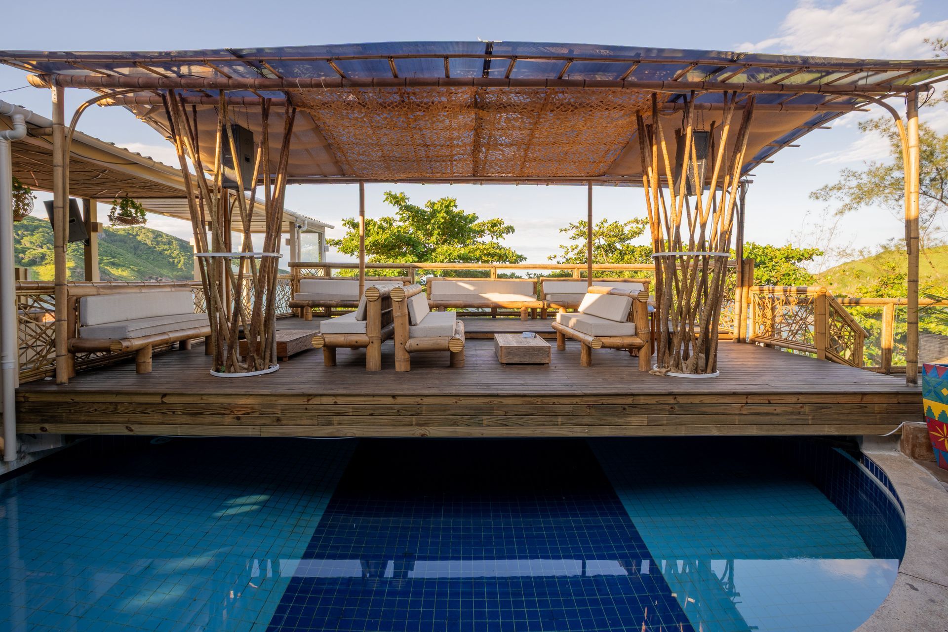 Restaurante branco com piscina em uma encosta, com outros edifícios e uma estrada visíveis. Dia ensolarado.