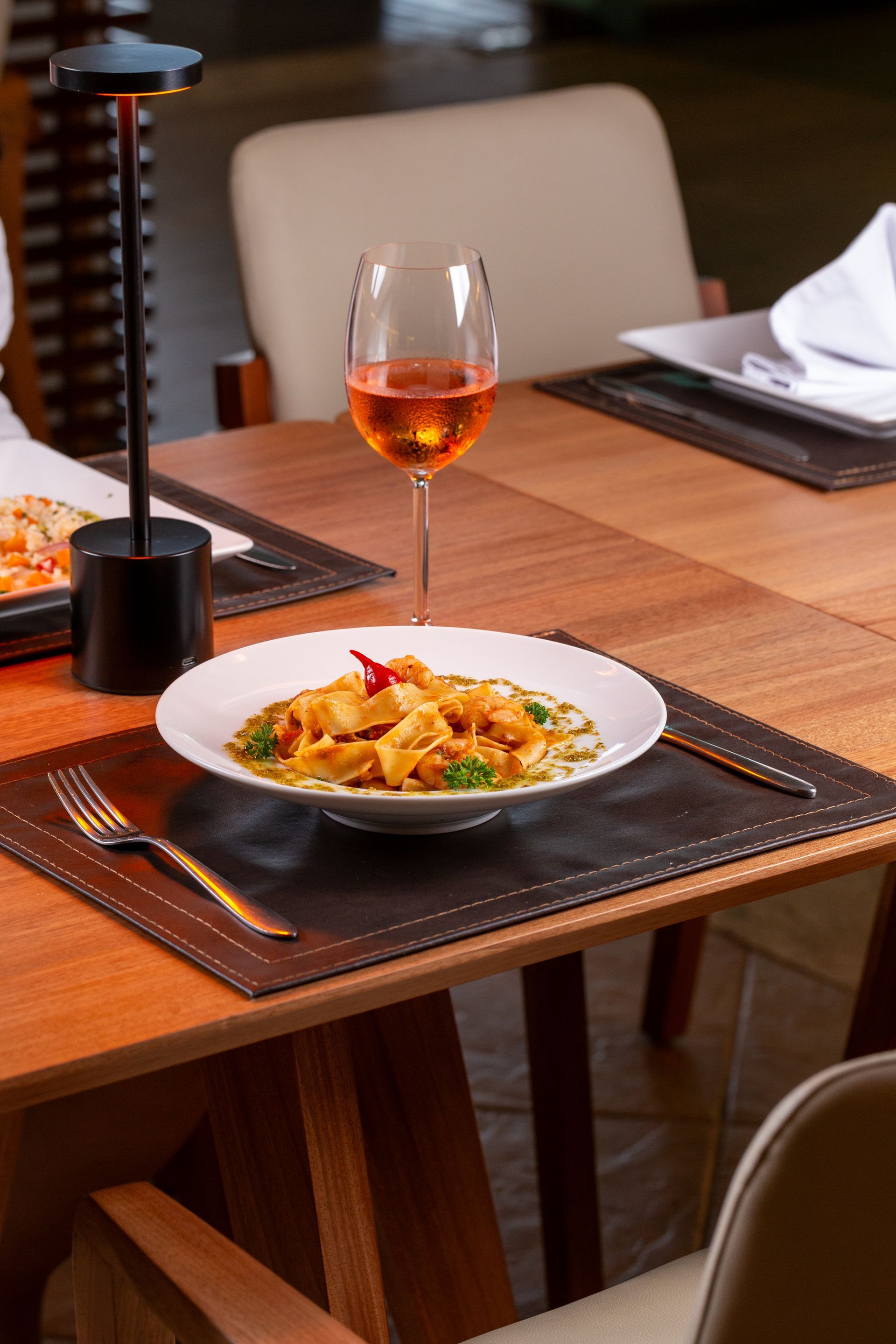 Prato de massa, taça de vinho e mesa posta em um restaurante com iluminação aconchegante.