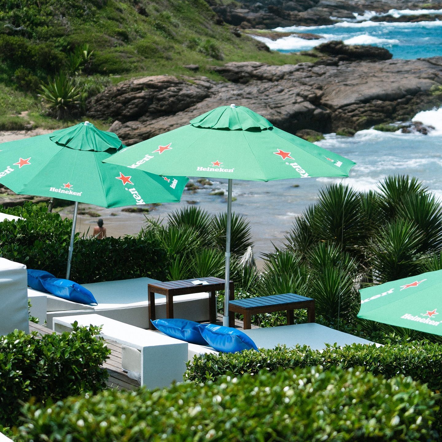 Cena de praia com guarda-sóis verdes da Heineken, espreguiçadeiras brancas e vista para o mar.