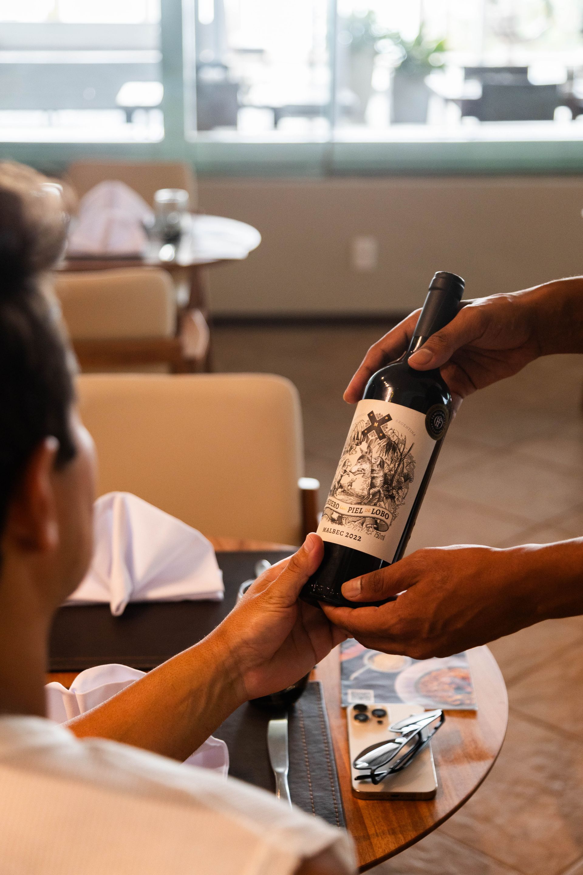 Pessoa que recebe uma garrafa de vinho de alguém em uma mesa de restaurante.