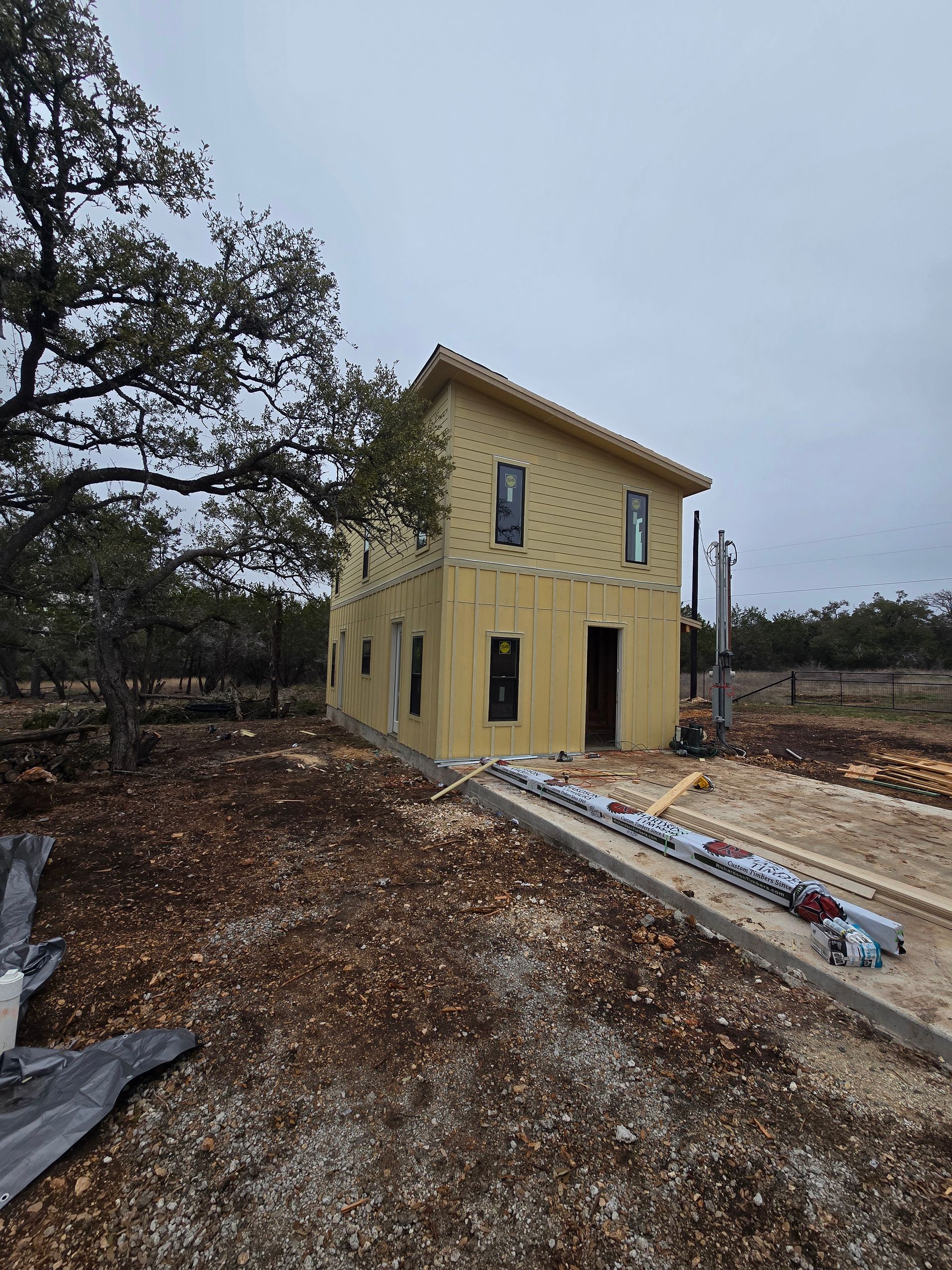 Two-story house under construction, yellow siding, windows, dirt lot, cloudy sky.