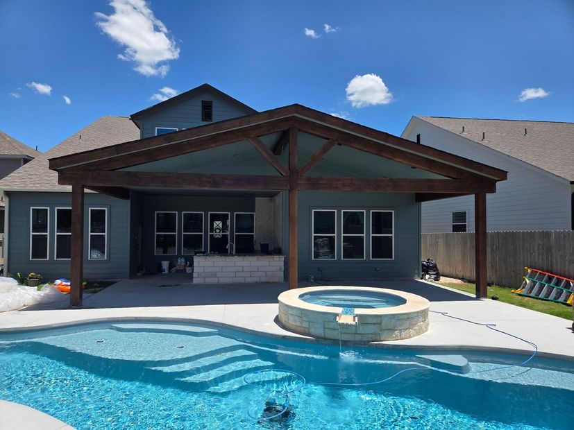 Outdoor patio with blue ceiling and brown wooden beams. Backyard with a fence and pool in the distance.
