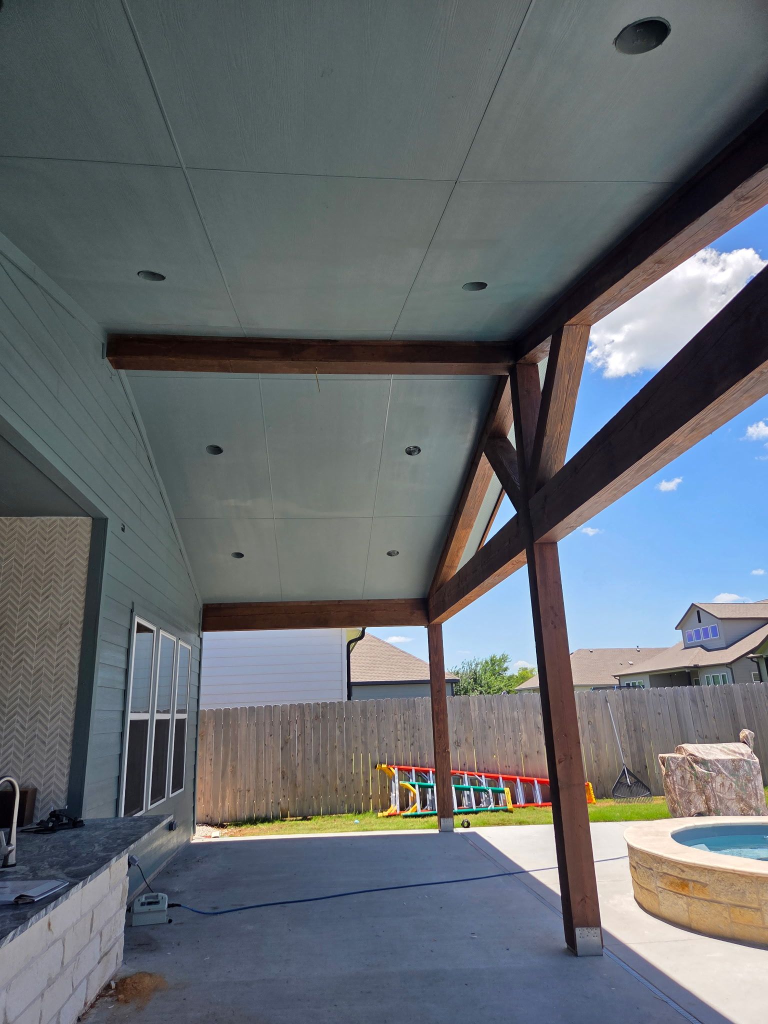 Patio with concrete floor, dark brown beams, and a light blue ceiling.