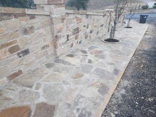 Stone walkway and wall, light brown and tan, next to a street.