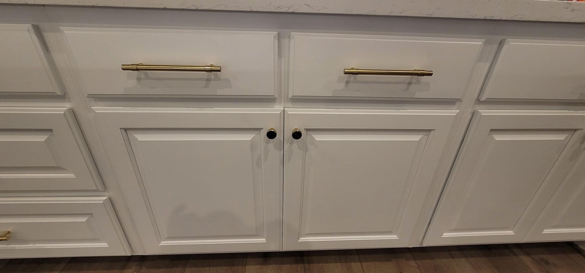 White kitchen cabinets with gold handles, and a dark knob.