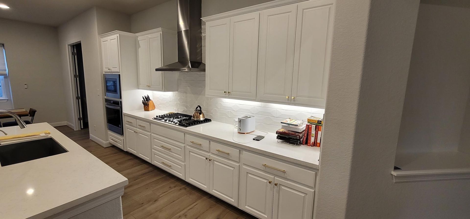 Kitchen with white cabinets, counters, and appliances. Features a stovetop, vent hood, and island.