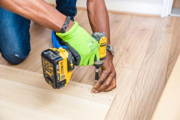 Person using a power drill to install or repair wooden flooring.