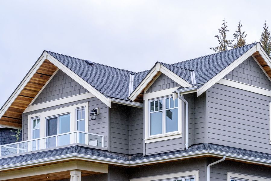 Gray house with white trim, a balcony, and a dark blue roof against a cloudy sky.