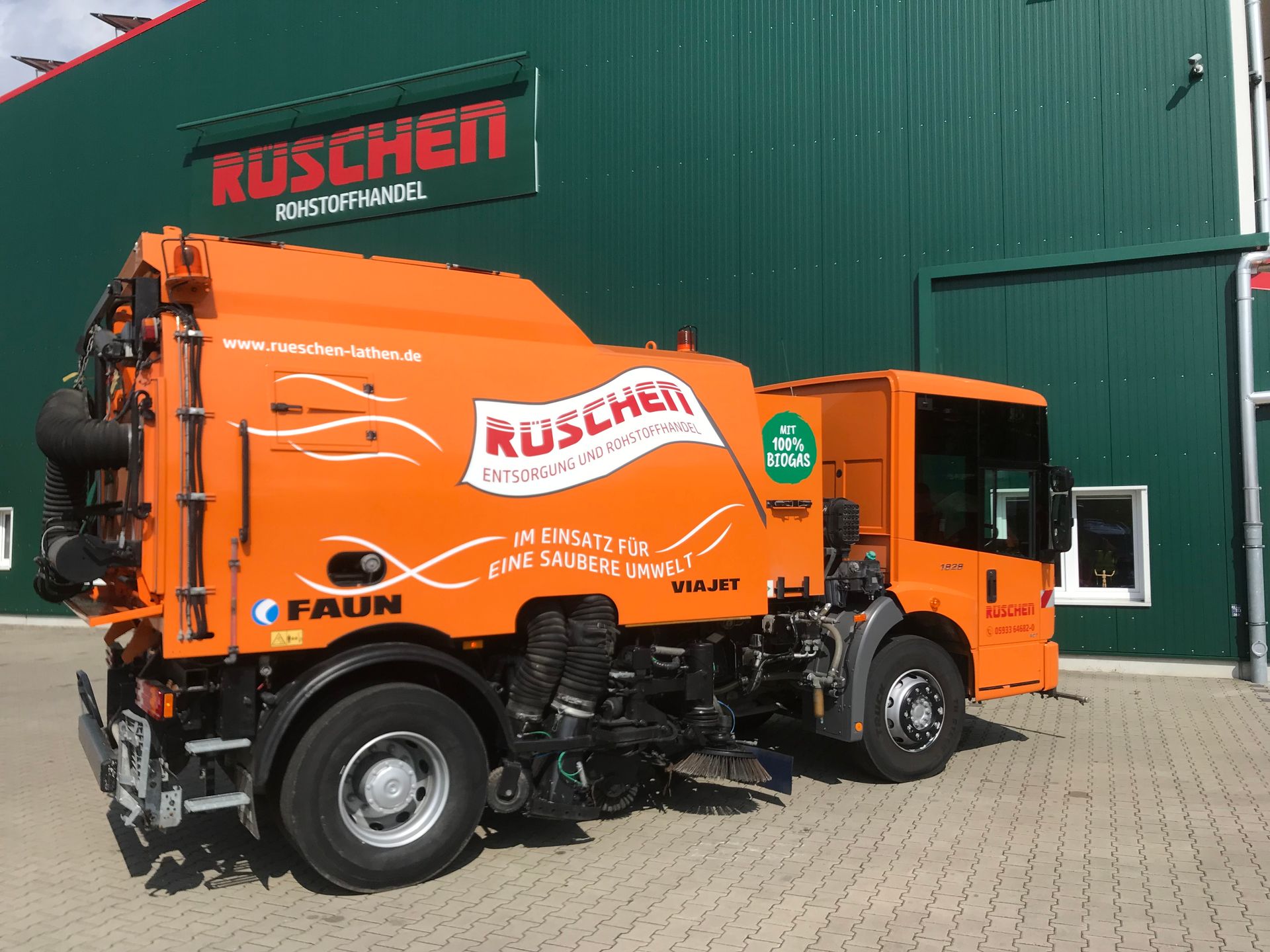Eine orangefarbene Kehrmaschine steht vor einem grünen Gebäude.