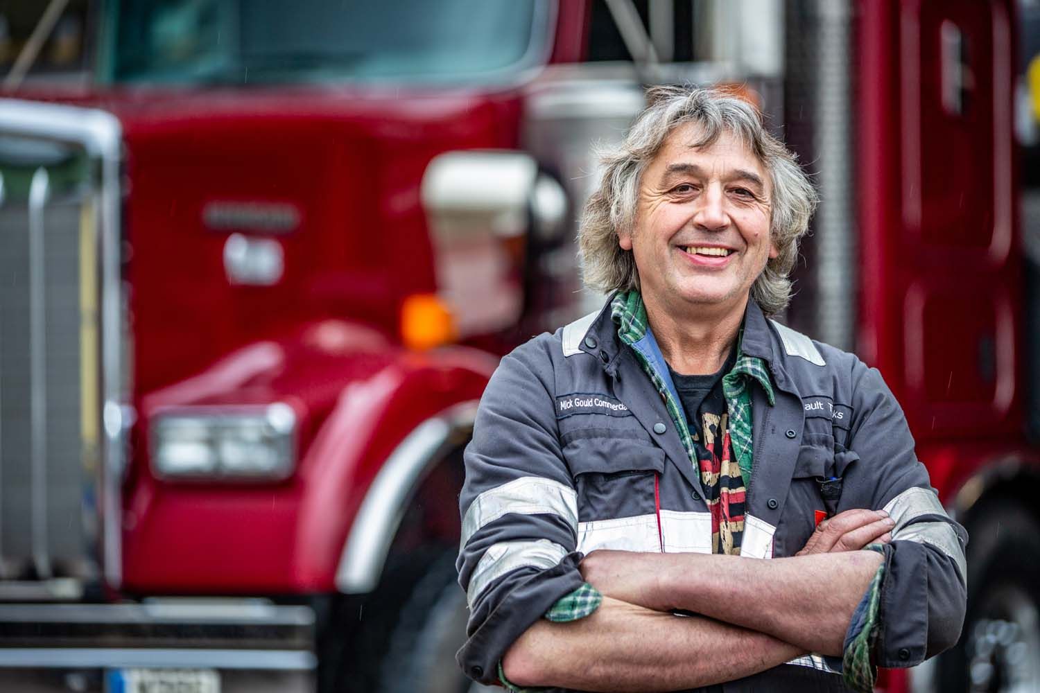 Smiling photograph of a person with folded arms standing in front of a red truck