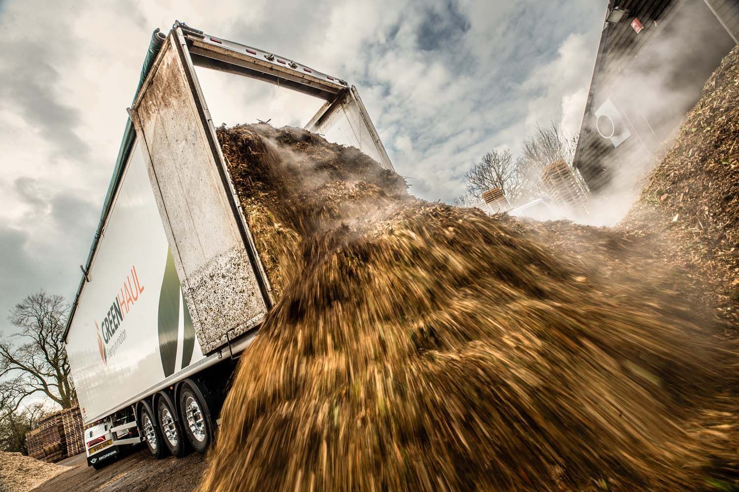 Impactful lorry photography featuring dump truck unloading a cascade of brown gravel, sending debris flying outdoors.