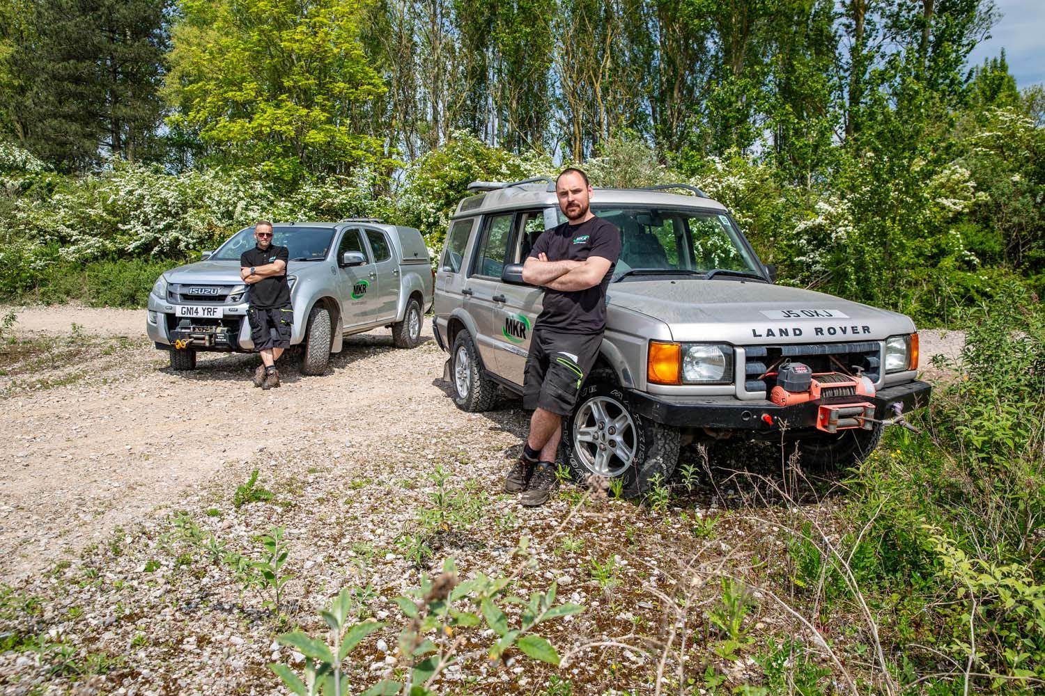 Two off-road SUVs on a gravel trail with a person standing in front of the nearest vehicle.