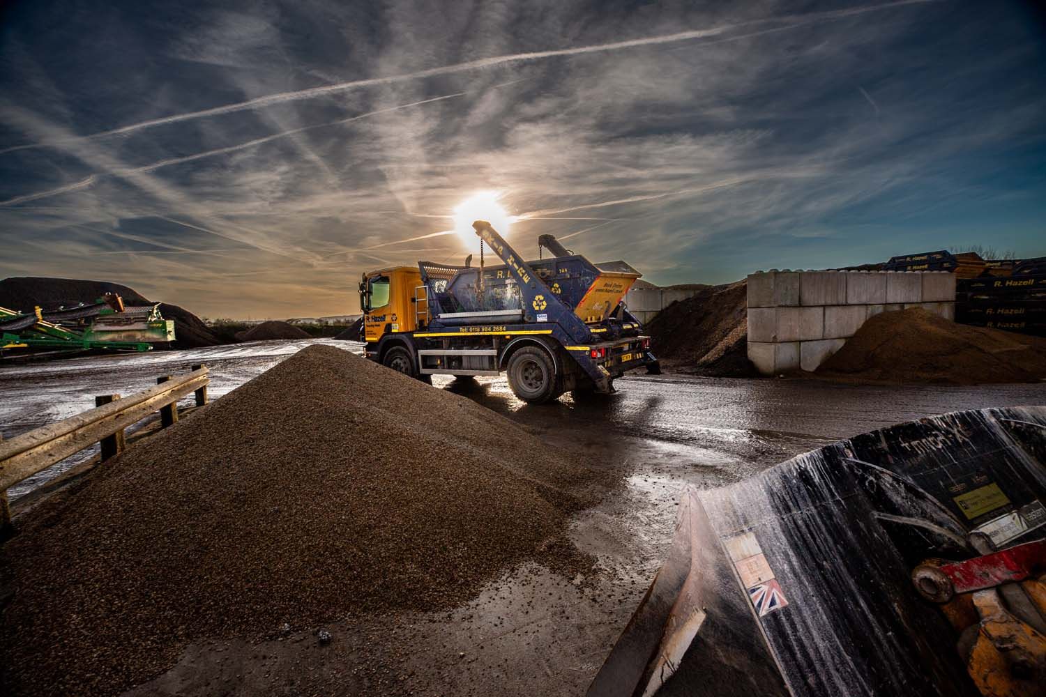 Construction lorry dumping gravel at a wet site during sunset