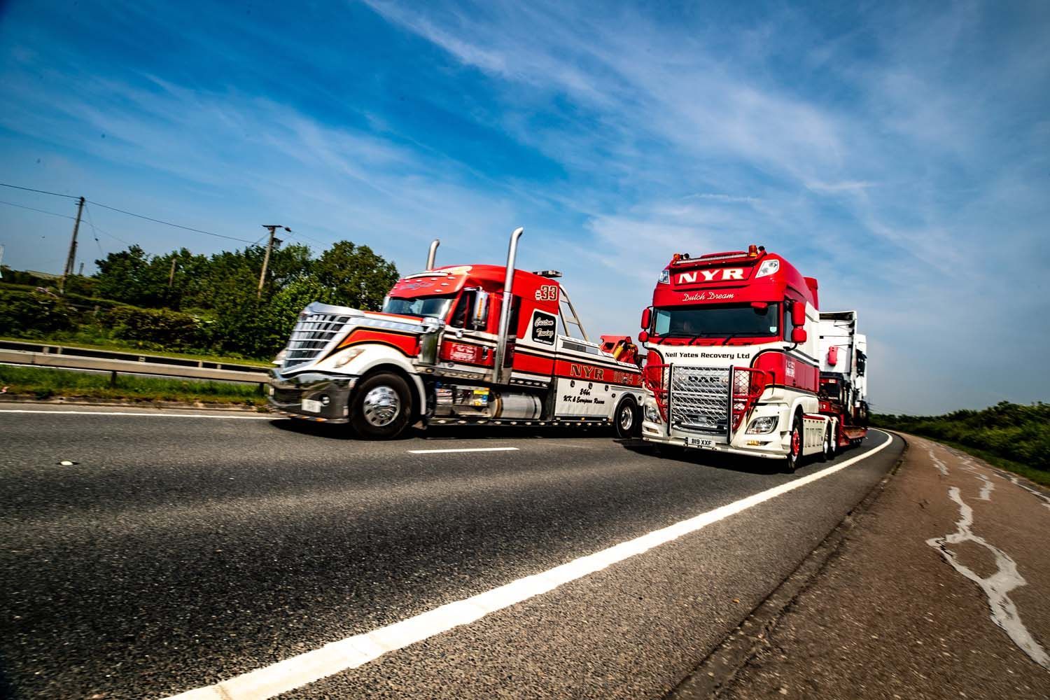 Two red trucks on a highway shoulder under a blue sky