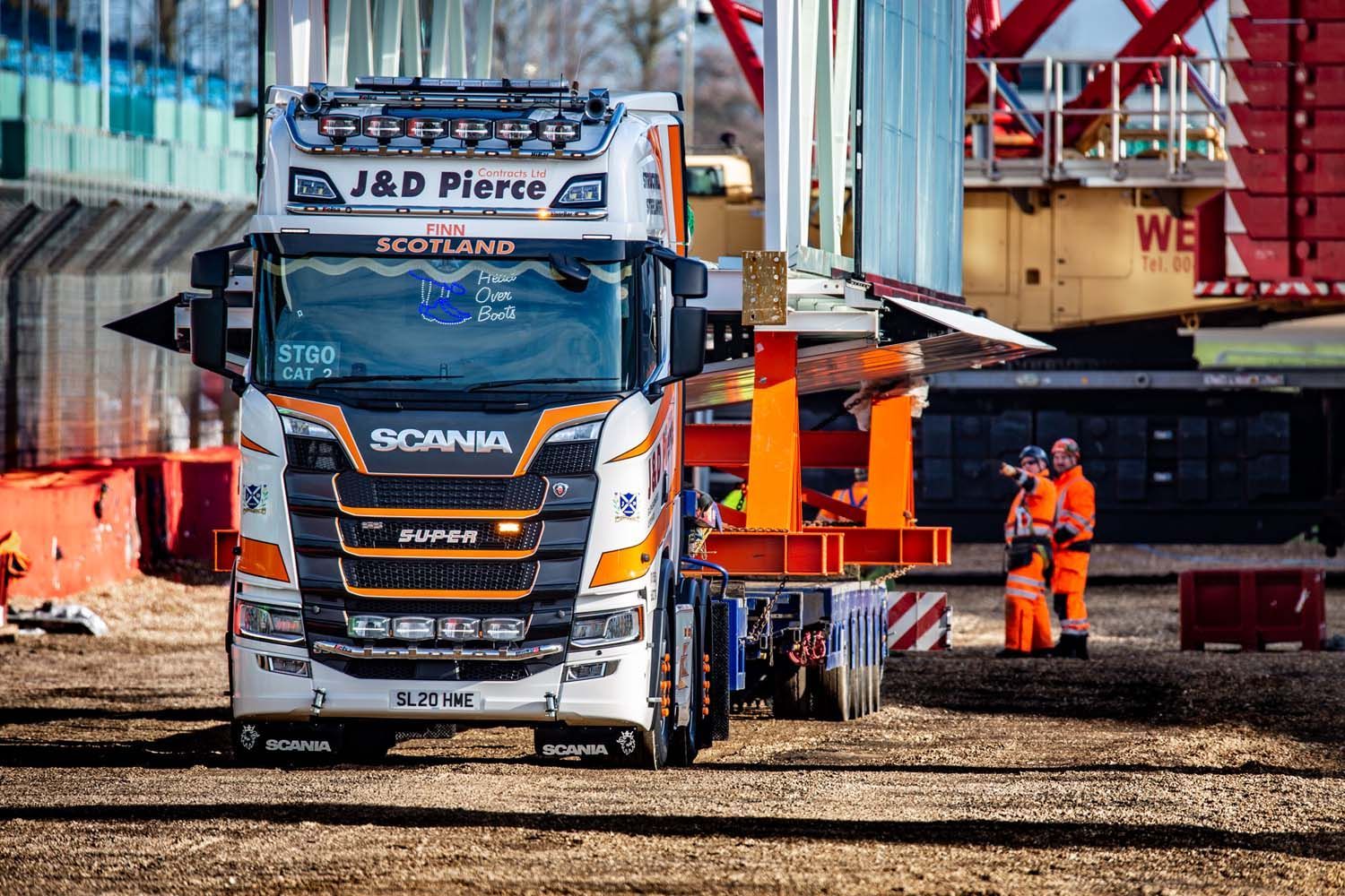 White Scania truck at a construction site with two workers in orange hi-vis gear