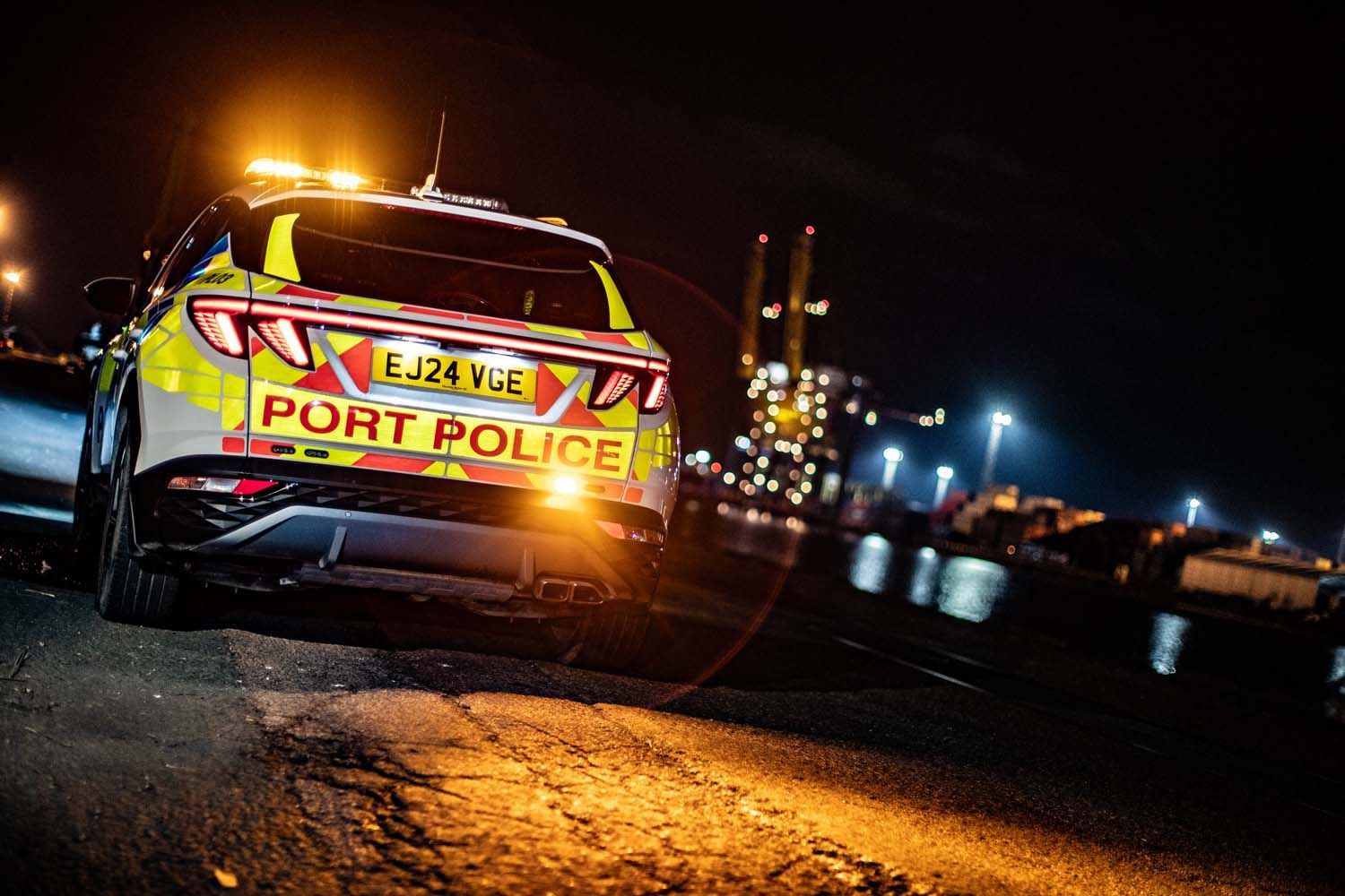 Nighttime Port Police SUV with flashing lights parked on a wet road near a harbor