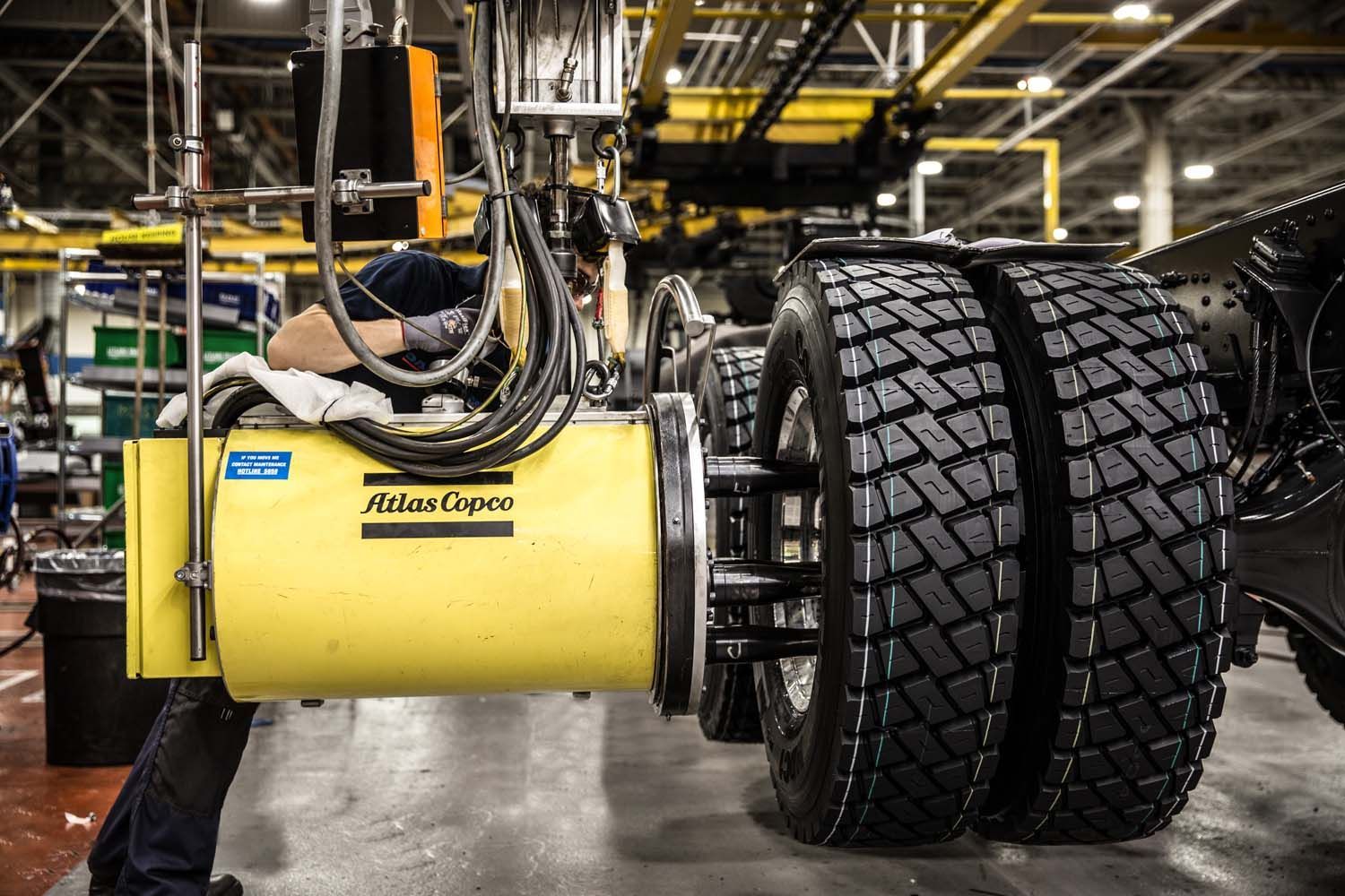 Close-up truck photography of yellow tire assembly machine beside a large tractor tire in a factory workshop