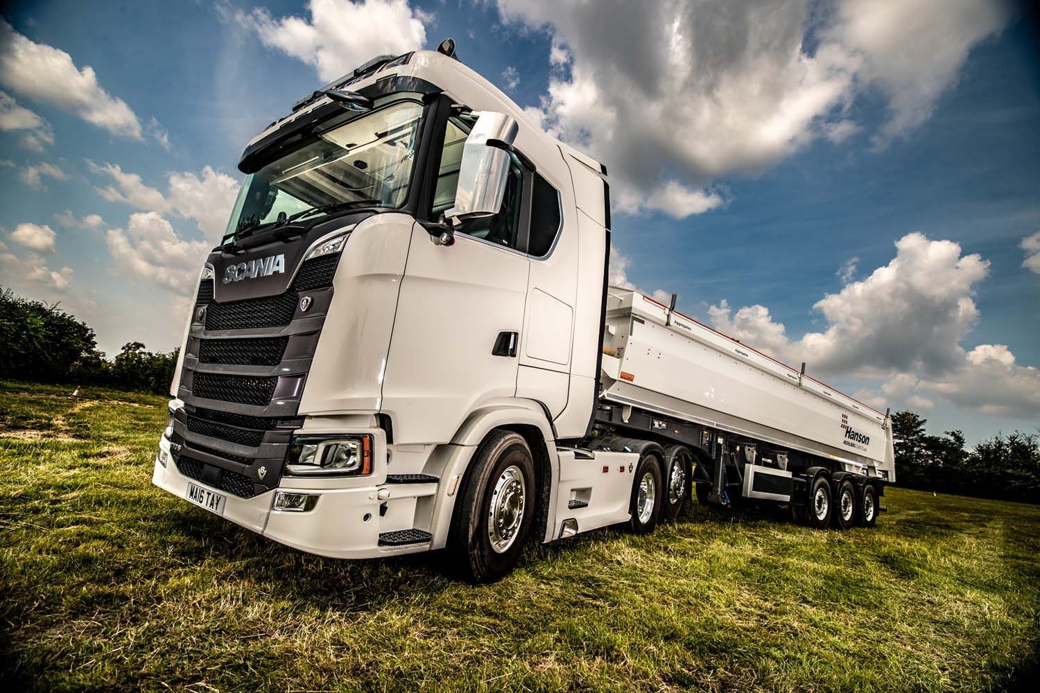 White tanker truck parked on grass under a cloudy blue sky