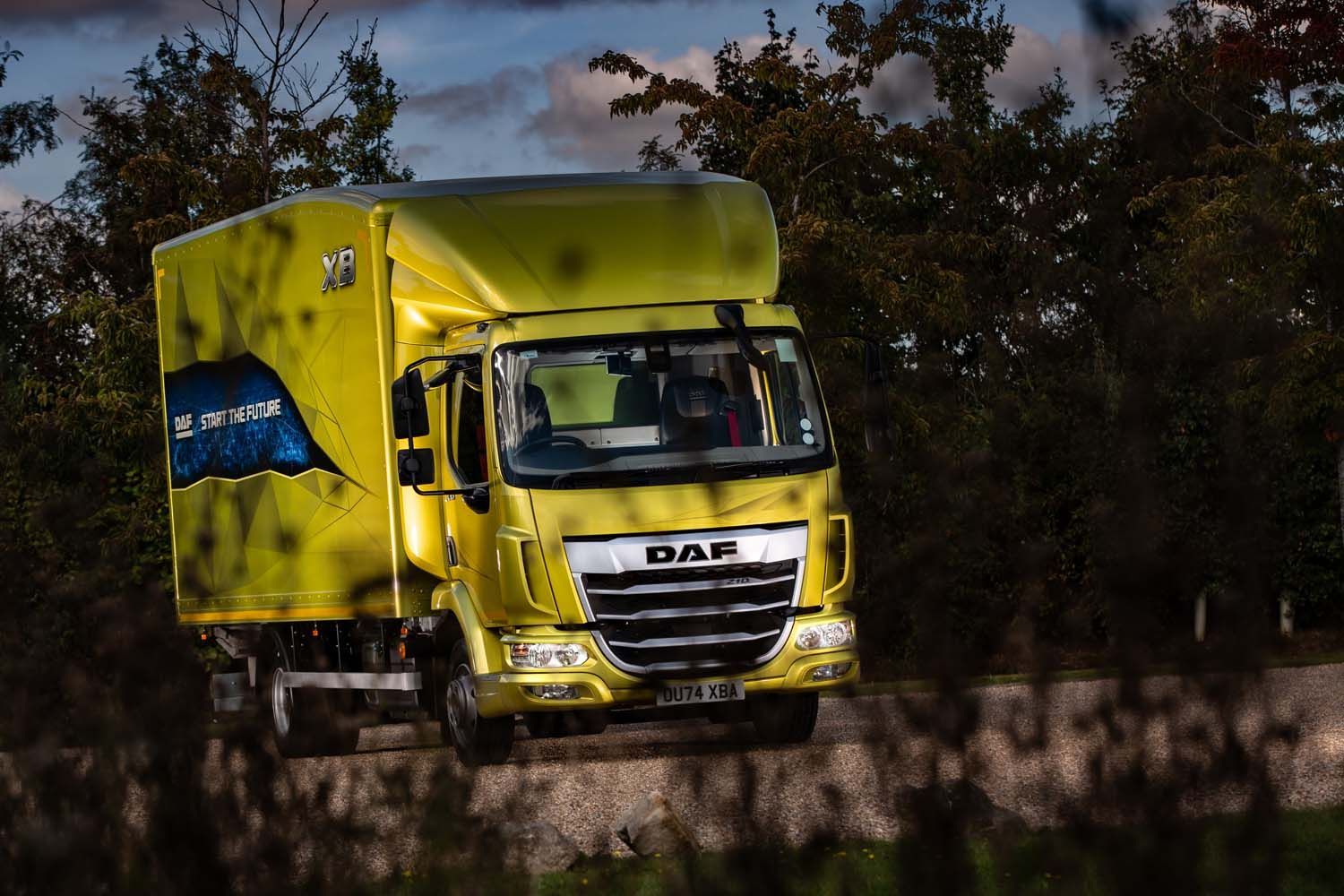 Yellow DHL delivery truck driving on a road with trees in the background
