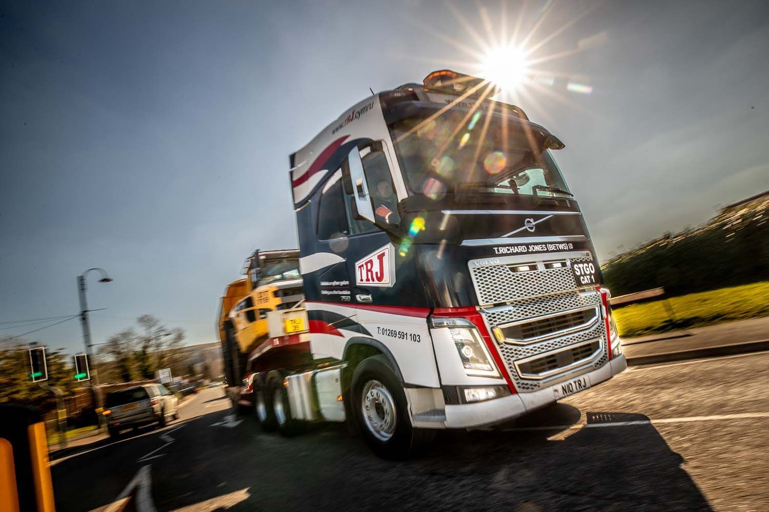 Red and white freight truck driving on a road in bright sunlight