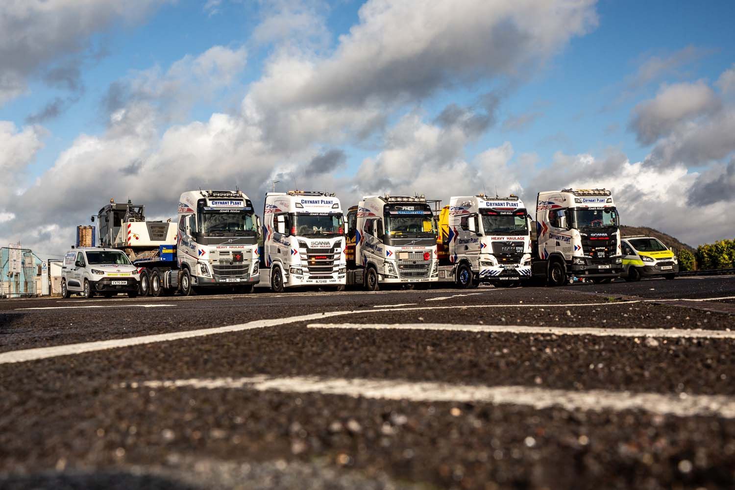 Lineup of colorful semi trucks on a road under a cloudy blue sky