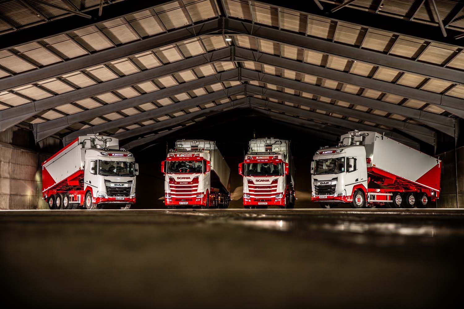 Four fire trucks lined up inside a warehouse garage under a high roof