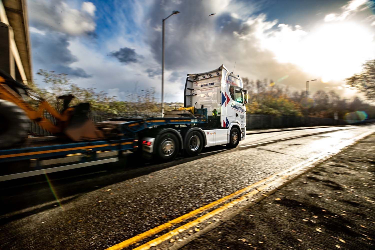 Truck hauling a damaged car on a sunlit road with motion blur and bright sky