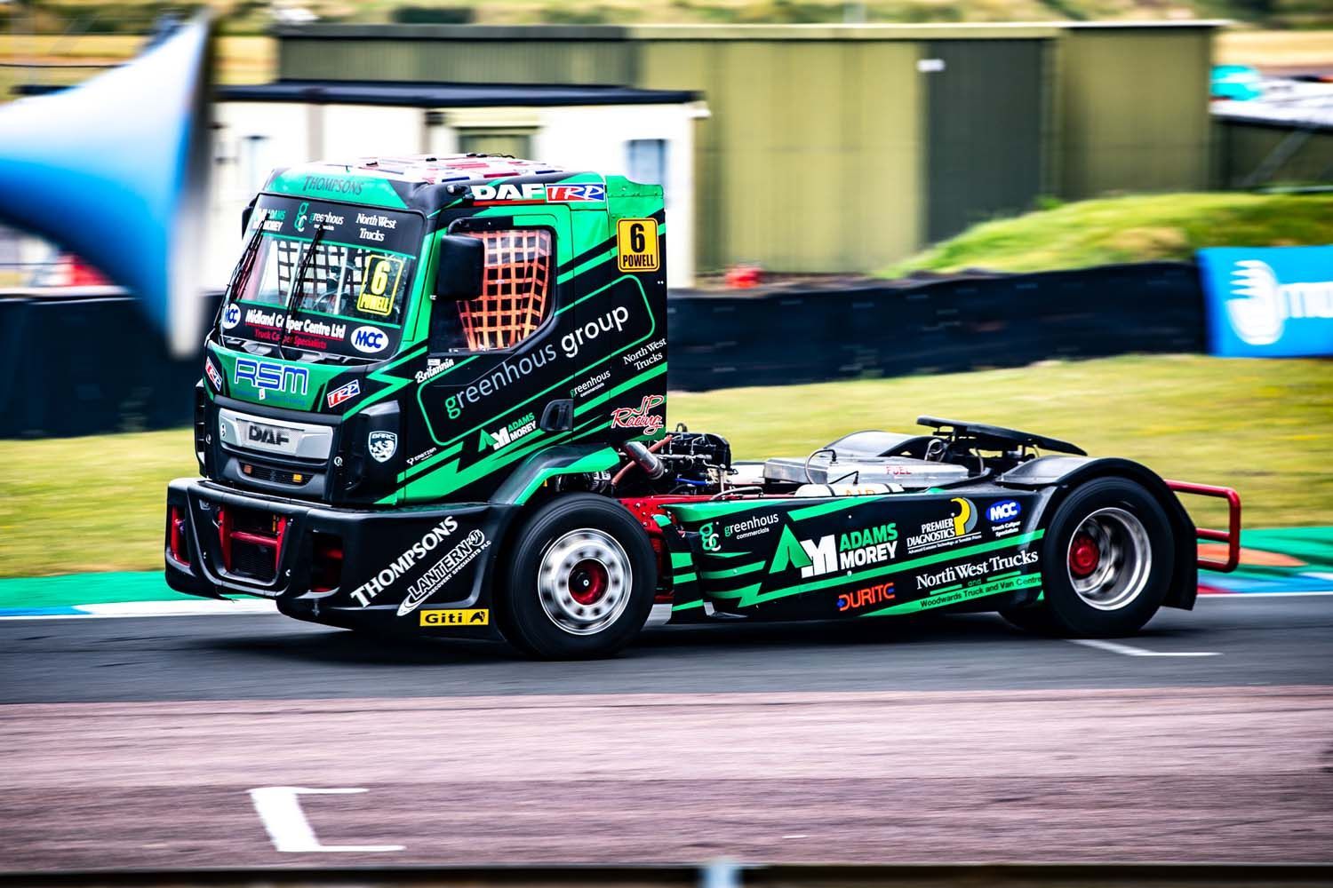 Black and green racing truck speeding on a track, motion blurred background