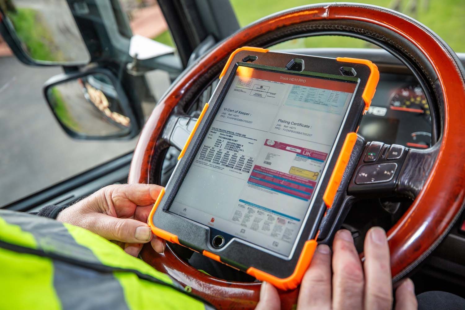 Interior truck photography of tablet mounted on a steering wheel showing a delivery app, with hands in a truck cab