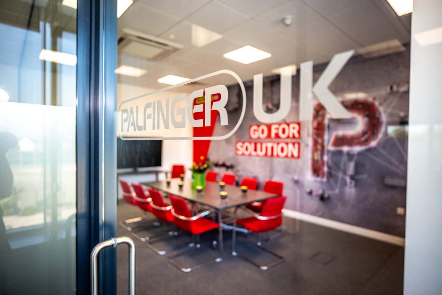 Photography of glass-walled conference room with red chairs, a table.