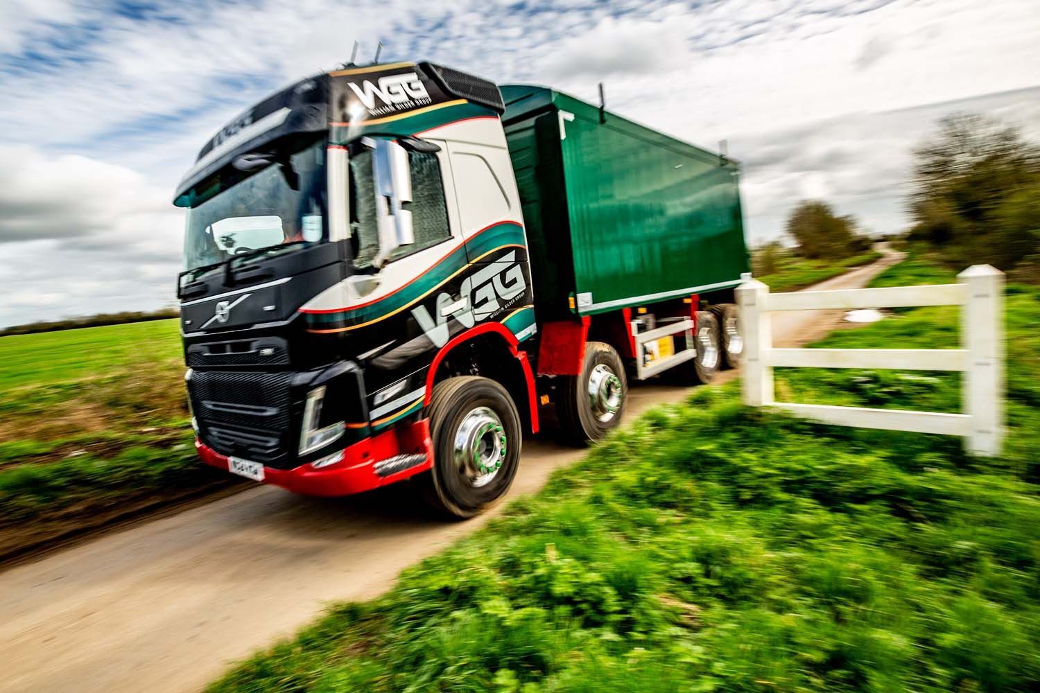 HGV photography featuring black and red lorry hauling a green trailer on a country road by a white fence