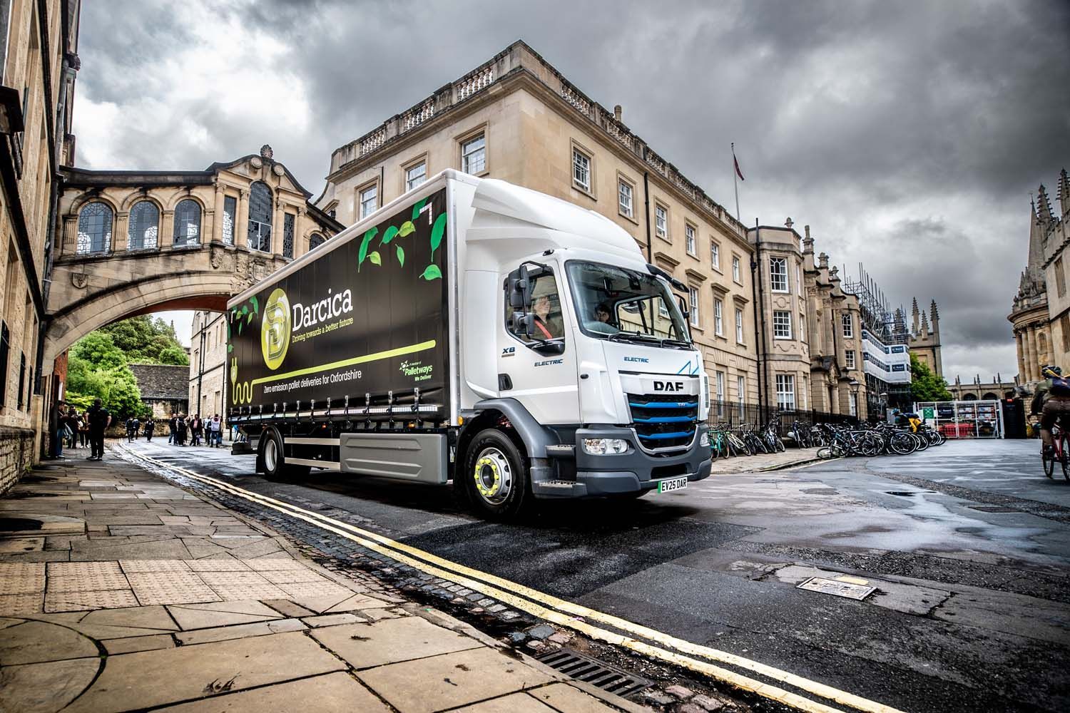 HGV photography of white delivery truck driving on a wet city street beside historic buildings and an archway.