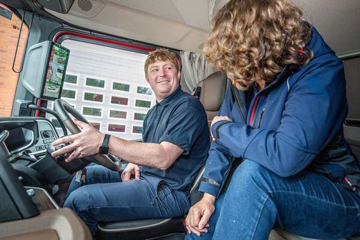 Truck driver demonstrating digital camera mirrors and safety technology inside a modern truck cab