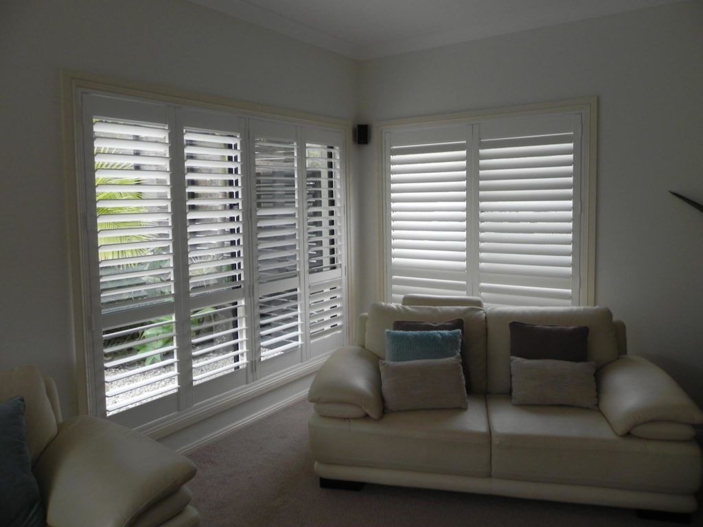 A Living Room with A Couch and Shutters on The Windows — Bay Blinds & Doors in Wyong, NSW