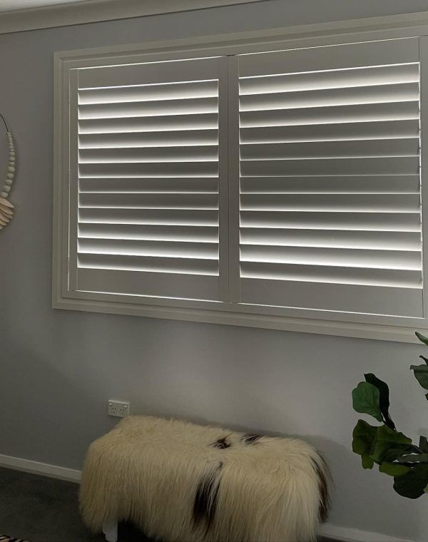 A Balcony with A Couch and Pillows and Shutters on The Windows — Bay Blinds & Doors in Morriset, NSW