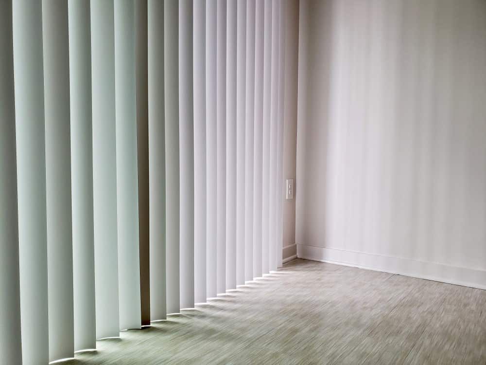 A Room with White Vertical Blinds on The Windows and A Wooden Floor — Bay Blinds & Doors in Bateau Bay, NSW