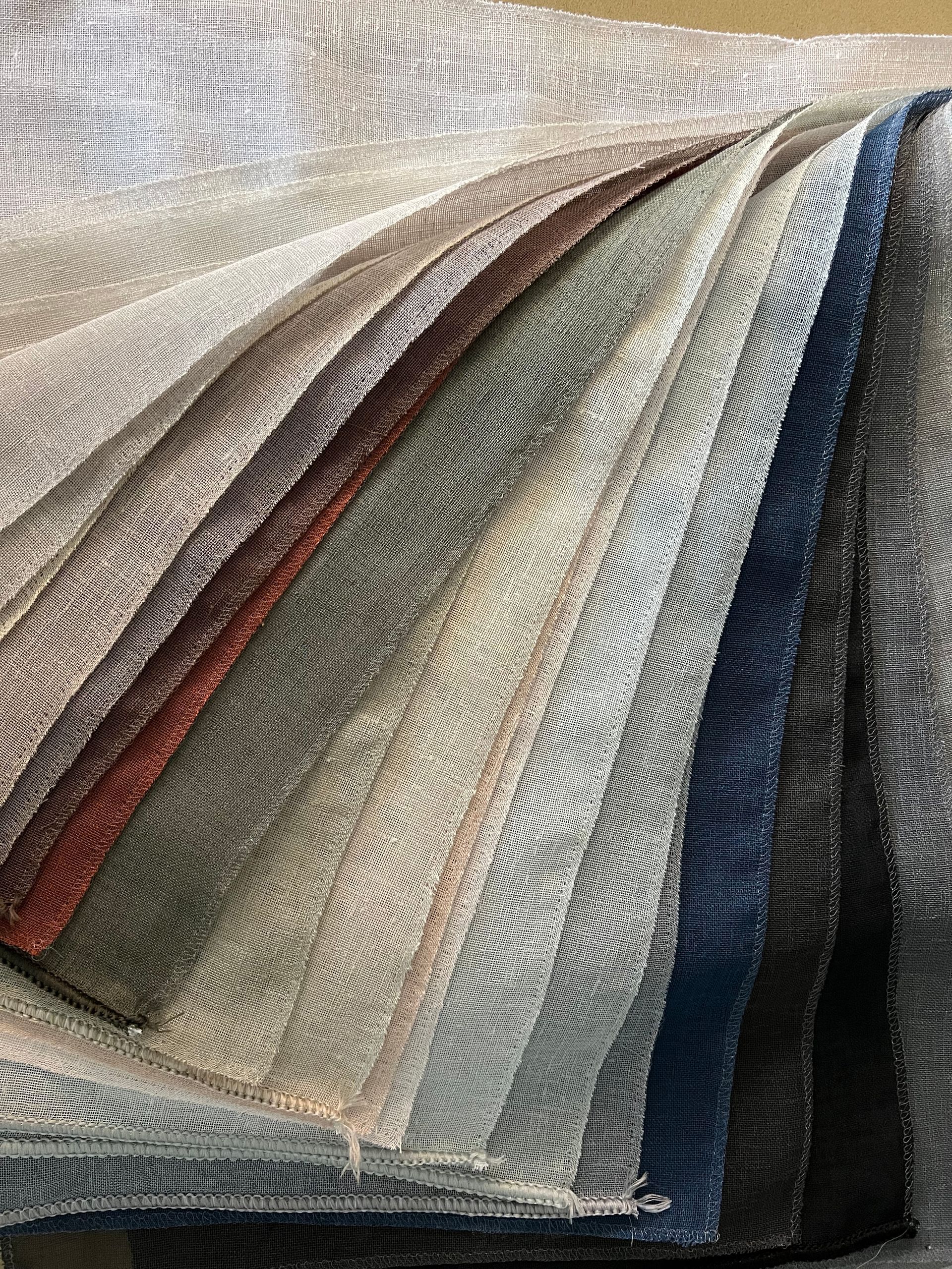 Stacked swatches of textured fabric in neutral, blue, gray, and black tones fanned out diagonally
