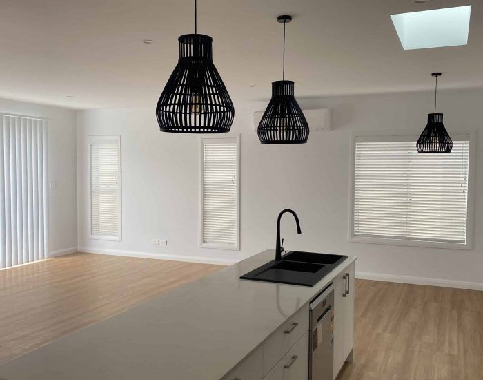 A Woman Is Cleaning a Window Blind with A Cloth — Bay Blinds & Doors in Bateau Bay, NSW