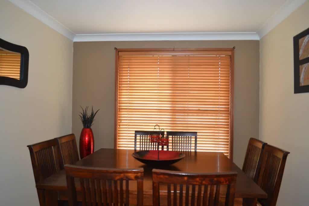 A Dining Room with A Table and Chairs and A Window with Blinds — Bay Blinds & Doors in Bateau Bay, NSW