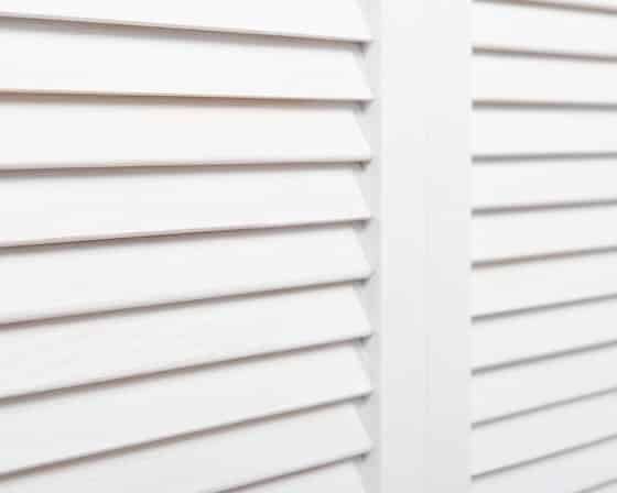 A Balcony with A Couch and Pillows and Shutters on The Windows — Bay Blinds & Doors in Wyee, NSW