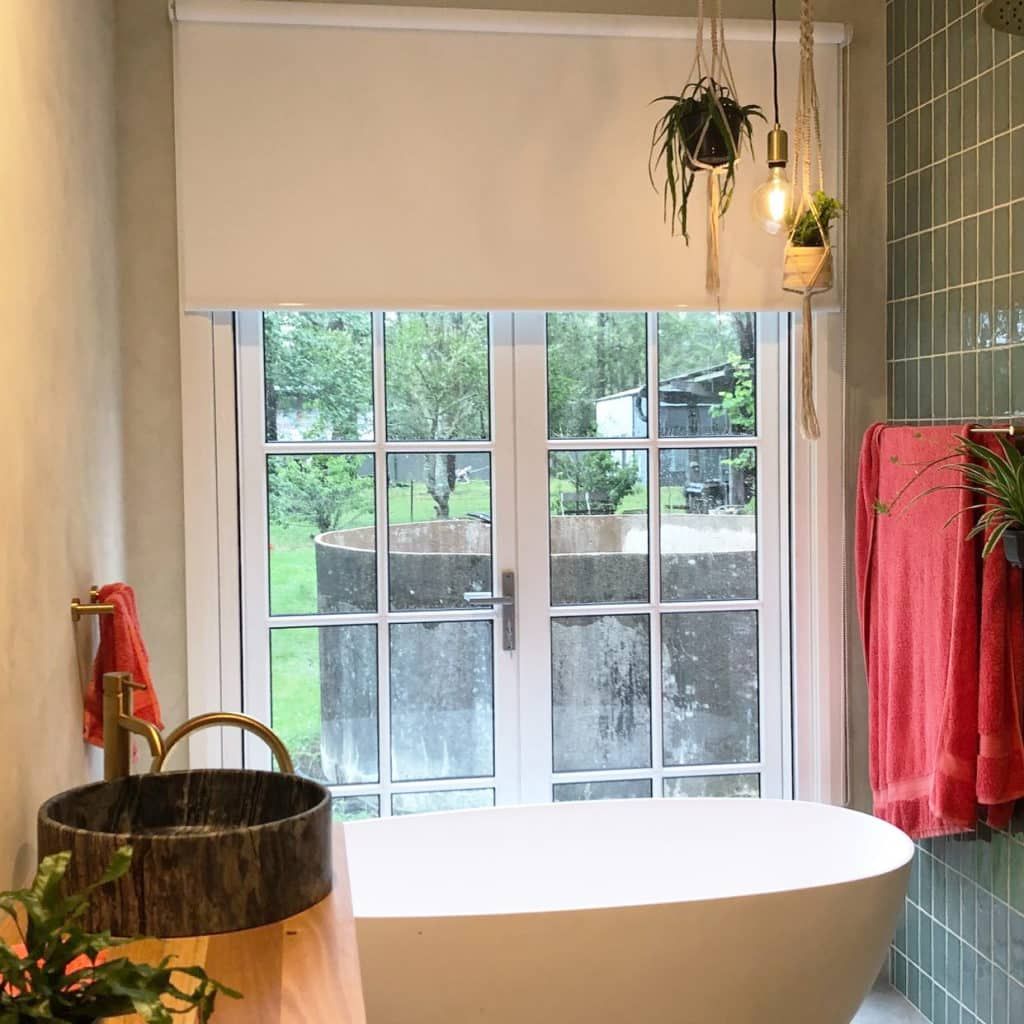 A Gray Roman Shade Is Hanging on A Window in A Room — Bay Blinds & Doors in Lake Munmorah, NSW