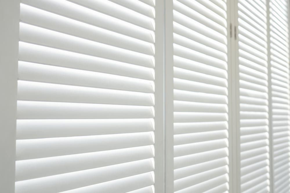 A Balcony with A Couch and Pillows and Shutters on The Windows — Bay Blinds & Doors in Wamberal, NSW