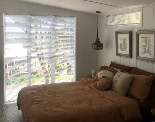 A Bedroom with A Large Bed and A Sliding Glass Door — Bay Blinds & Doors in Erina, NSW