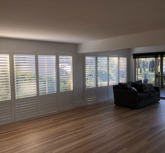 A Living Room with A Couch and Shutters on The Windows — Bay Blinds & Doors in Erina, NSW
