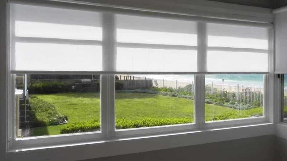 A Gray and White Striped Roman Shade Is Hanging on A Window — Bay Blinds & Doors in Wamberal, NSW